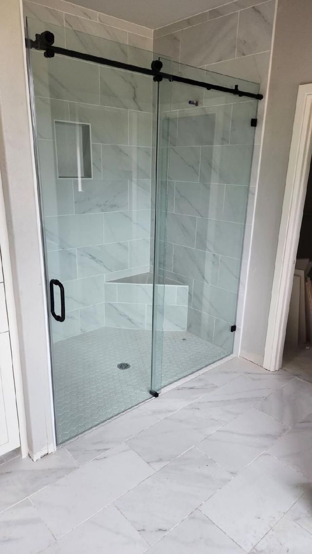 Glass walk-in shower with black hardware in a white tiled bathroom