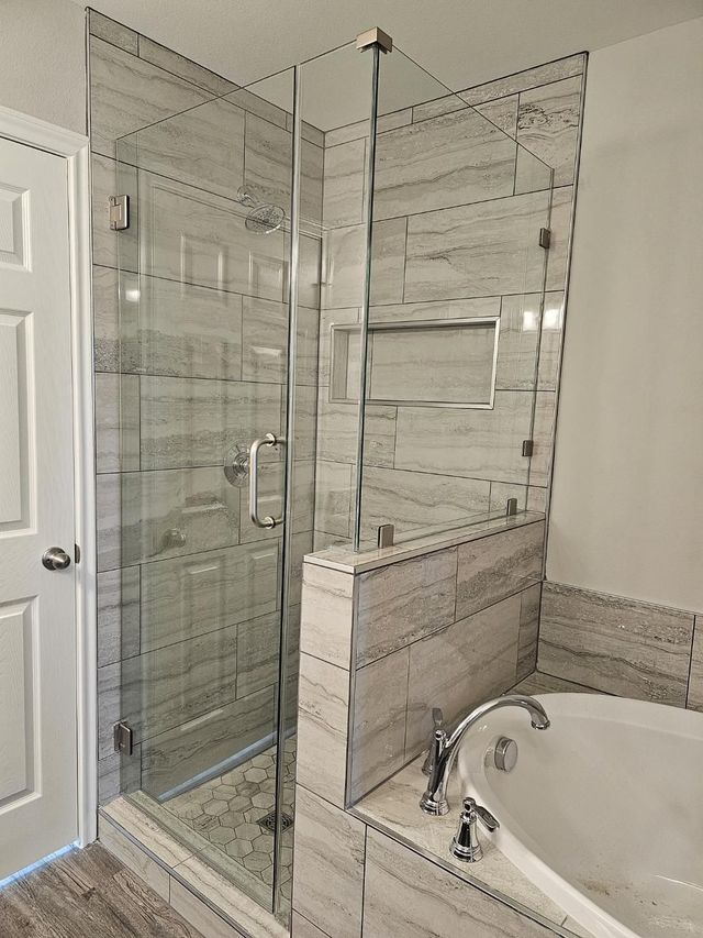 Bathroom with glass shower, tiled walls, and corner bathtub with chrome fixtures.
