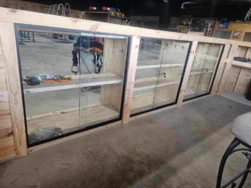 Three wooden-framed glass display cases lined up in a workshop or garage, with a concrete floor and tools in the background.
