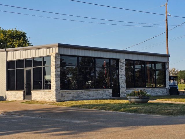 Small commercial building with large dark windows, stone facade, and metal awning by a road under a clear sky