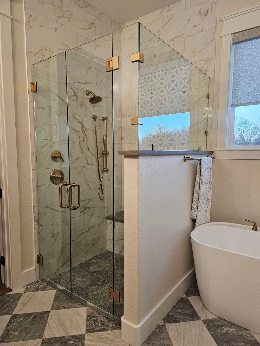 Modern bathroom with glass shower, tiled floor, and freestanding tub beside a window.