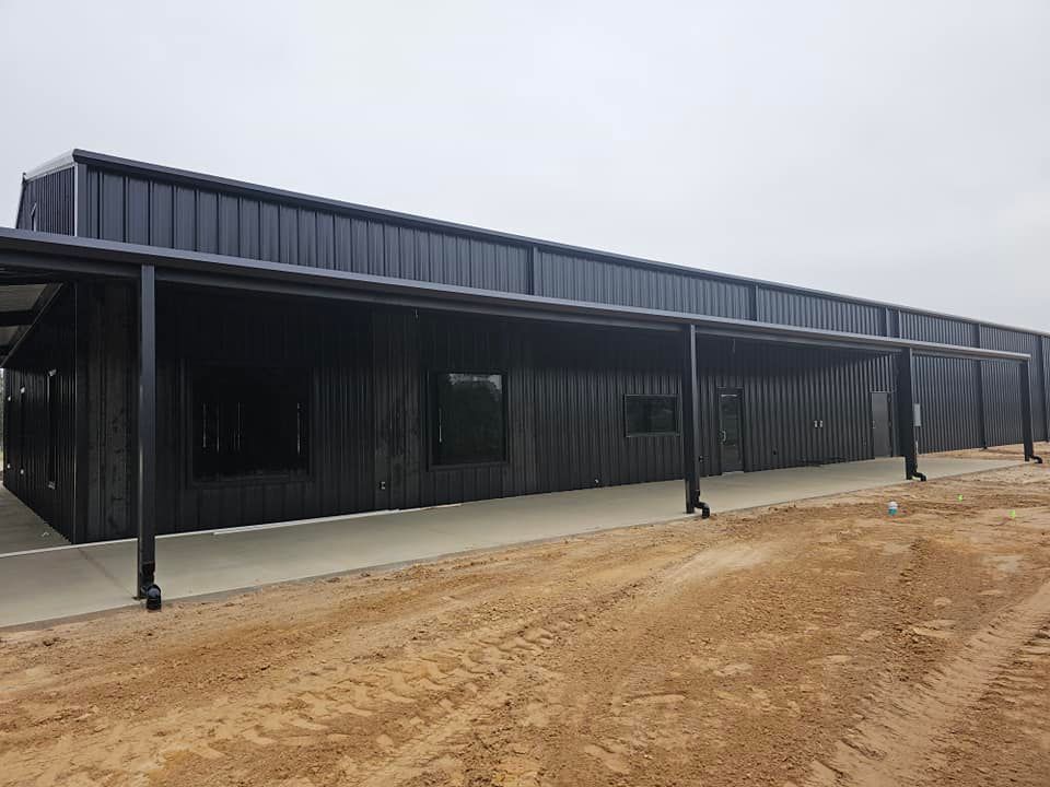 Long black metal building with covered walkway on a dirt lot under an overcast sky