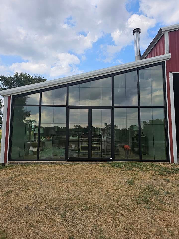 Modern house exterior with large black-framed glass wall and slanted red roof under cloudy sky