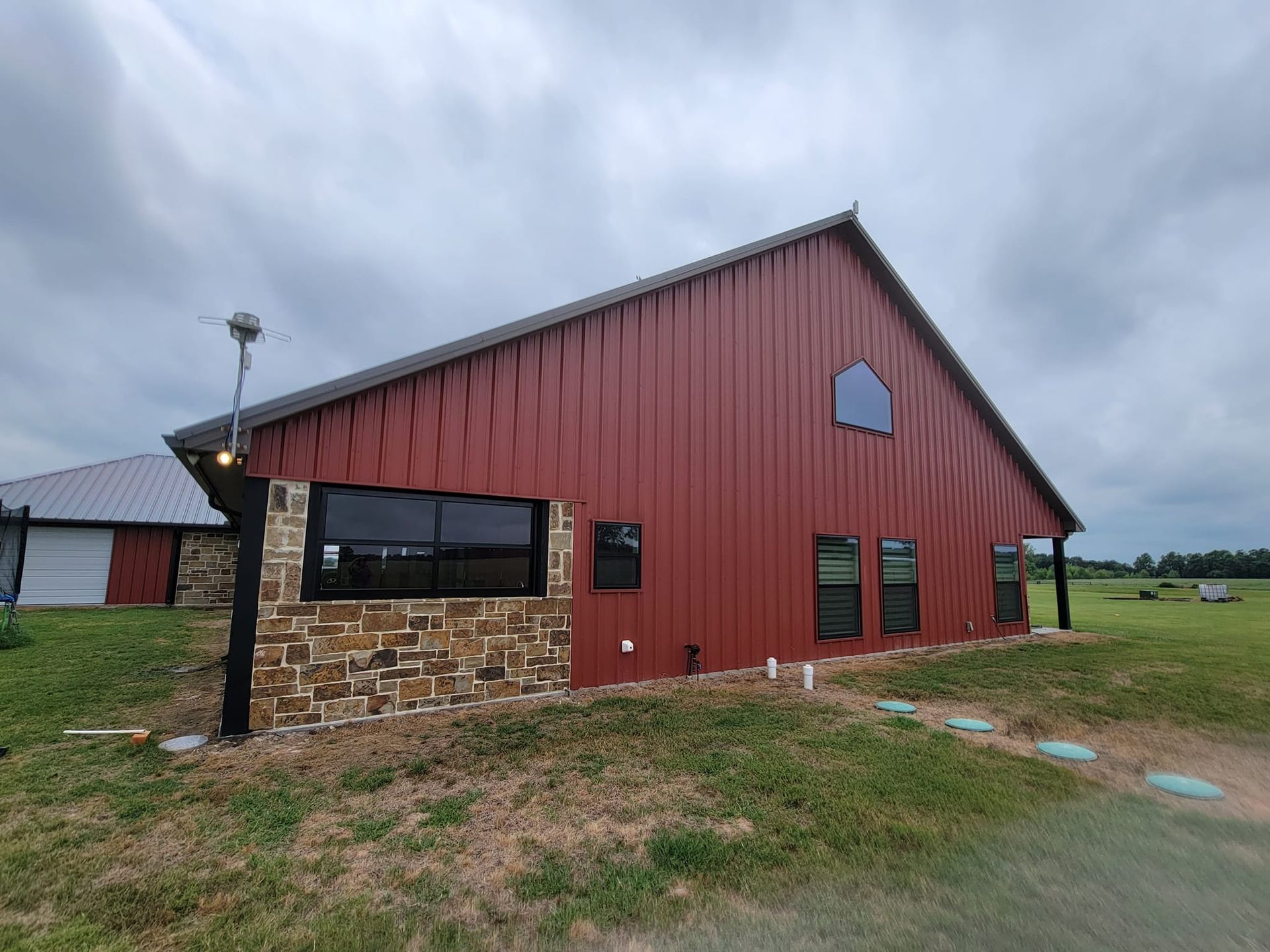 Red barn-style building with stone facade and large windows on a grassy lot under a cloudy sky