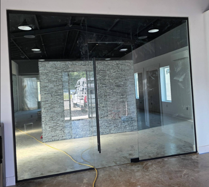 Glass partition wall inside an unfinished room with exposed ceiling, stone accent wall, and a yellow cord on the floor