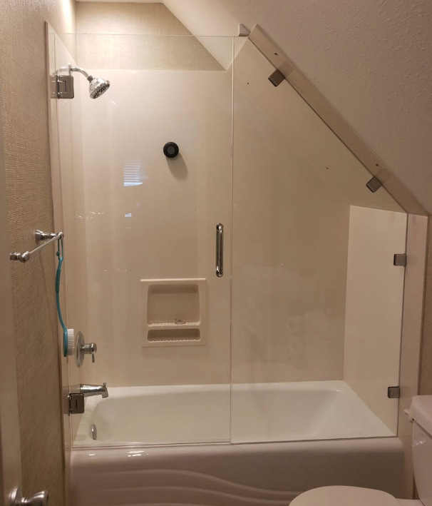 Glass-enclosed bathtub shower with bench, chrome fixtures, and slanted ceiling in a bathroom