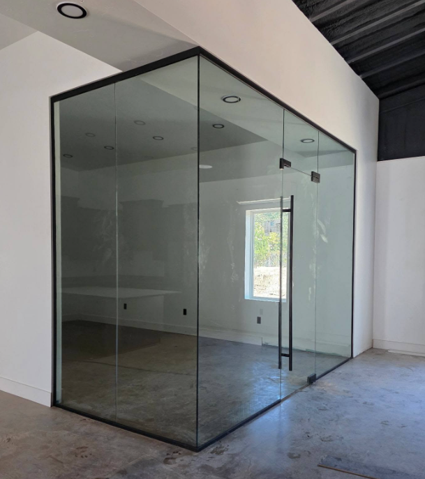 Glass-walled office room with black frame inside a white industrial space