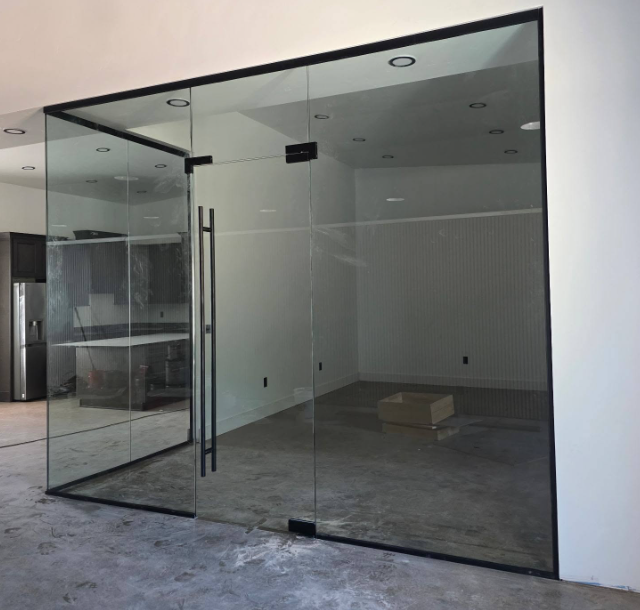 Empty glass storefront with a black metal frame and open door in a concrete-floored room