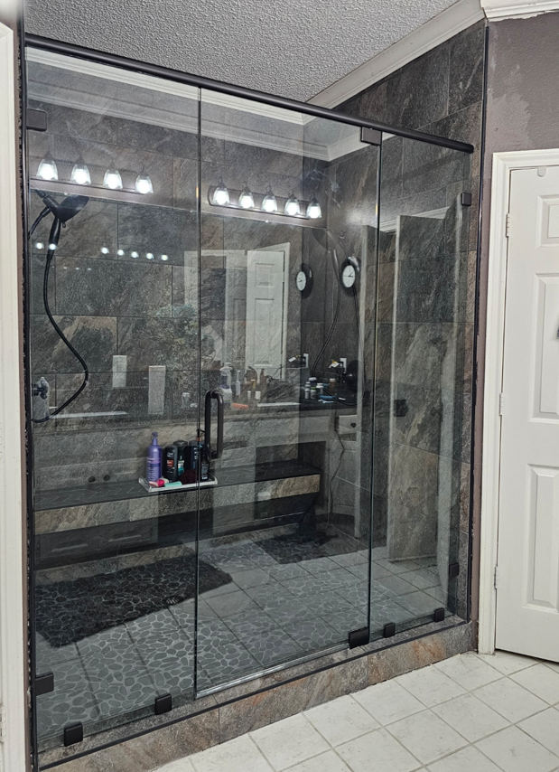 Glass walk-in shower with black metal frame and gray tile bathroom floor, viewed from outside the enclosure
