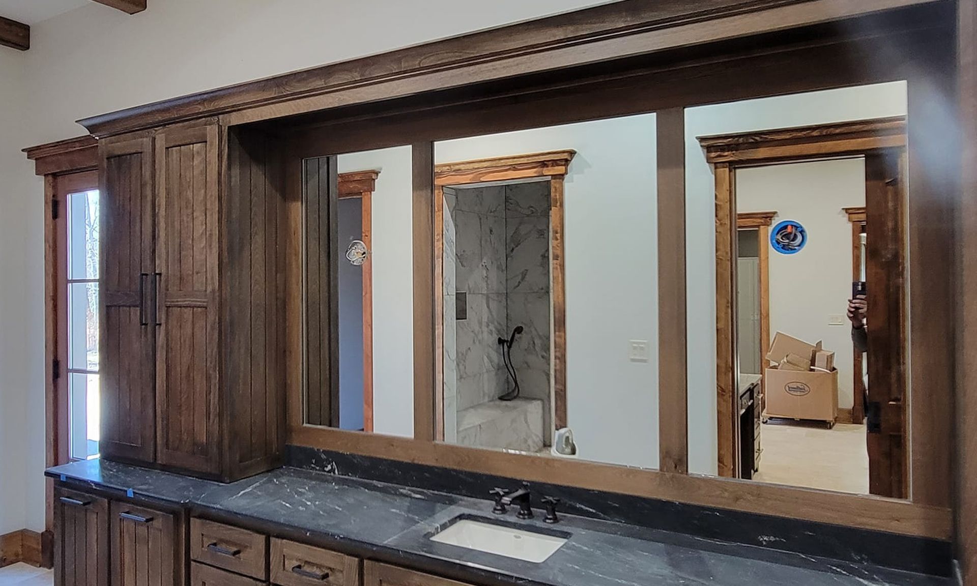 Wood-paneled bathroom vanity with three mirrors and dark countertop in a home interior