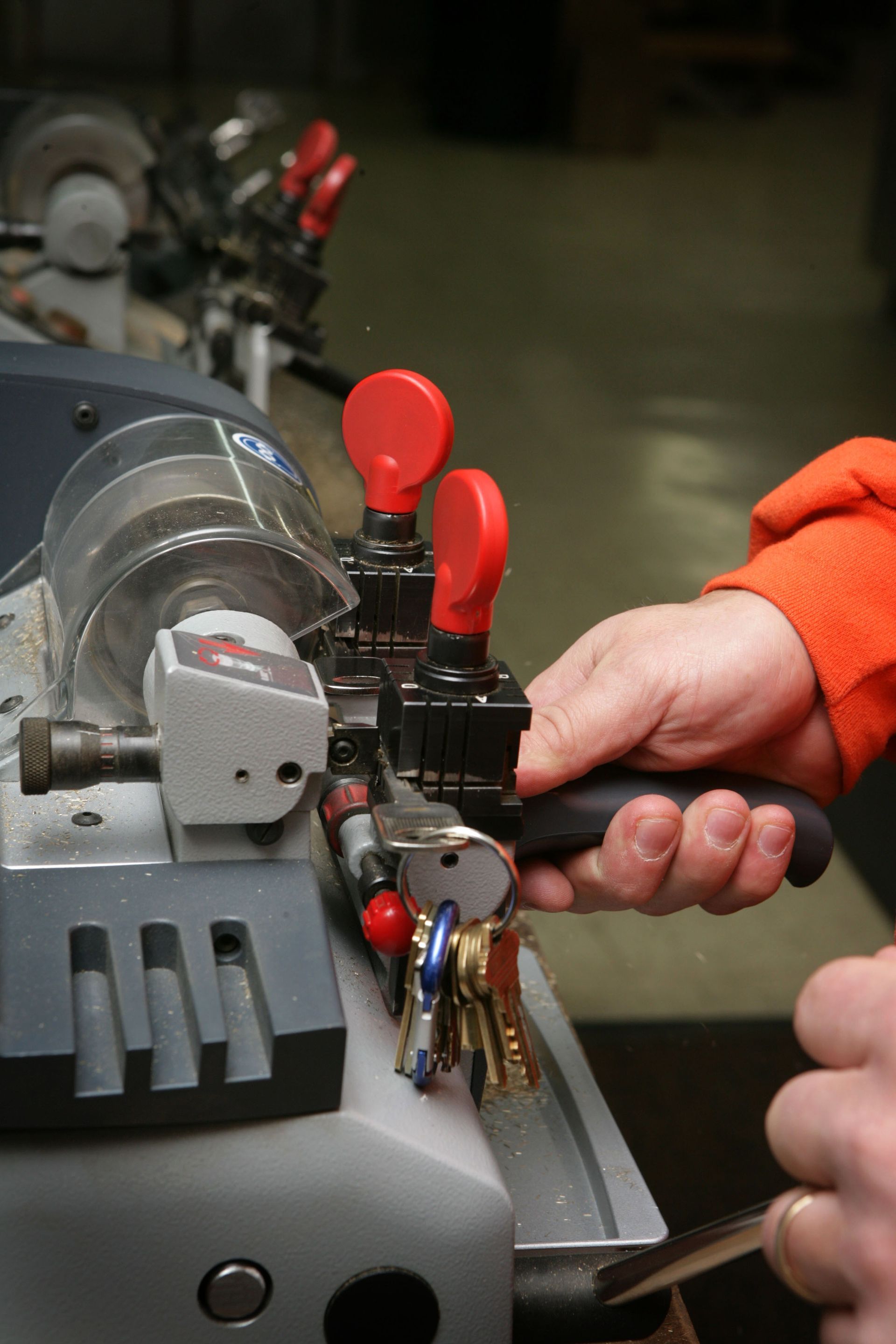 A person cutting keys on a key-cutting machine. The machine is gray, with red handles, and the person holds a key.