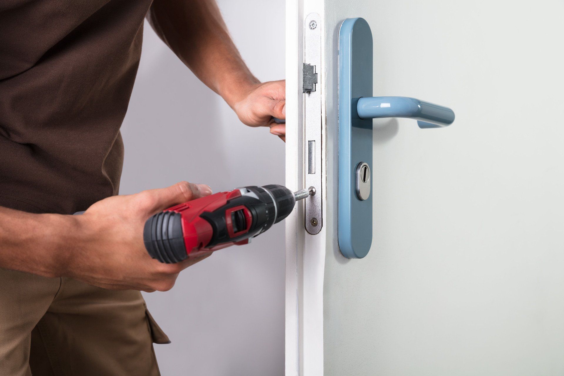 Person using a drill to install a blue door handle on a white door.