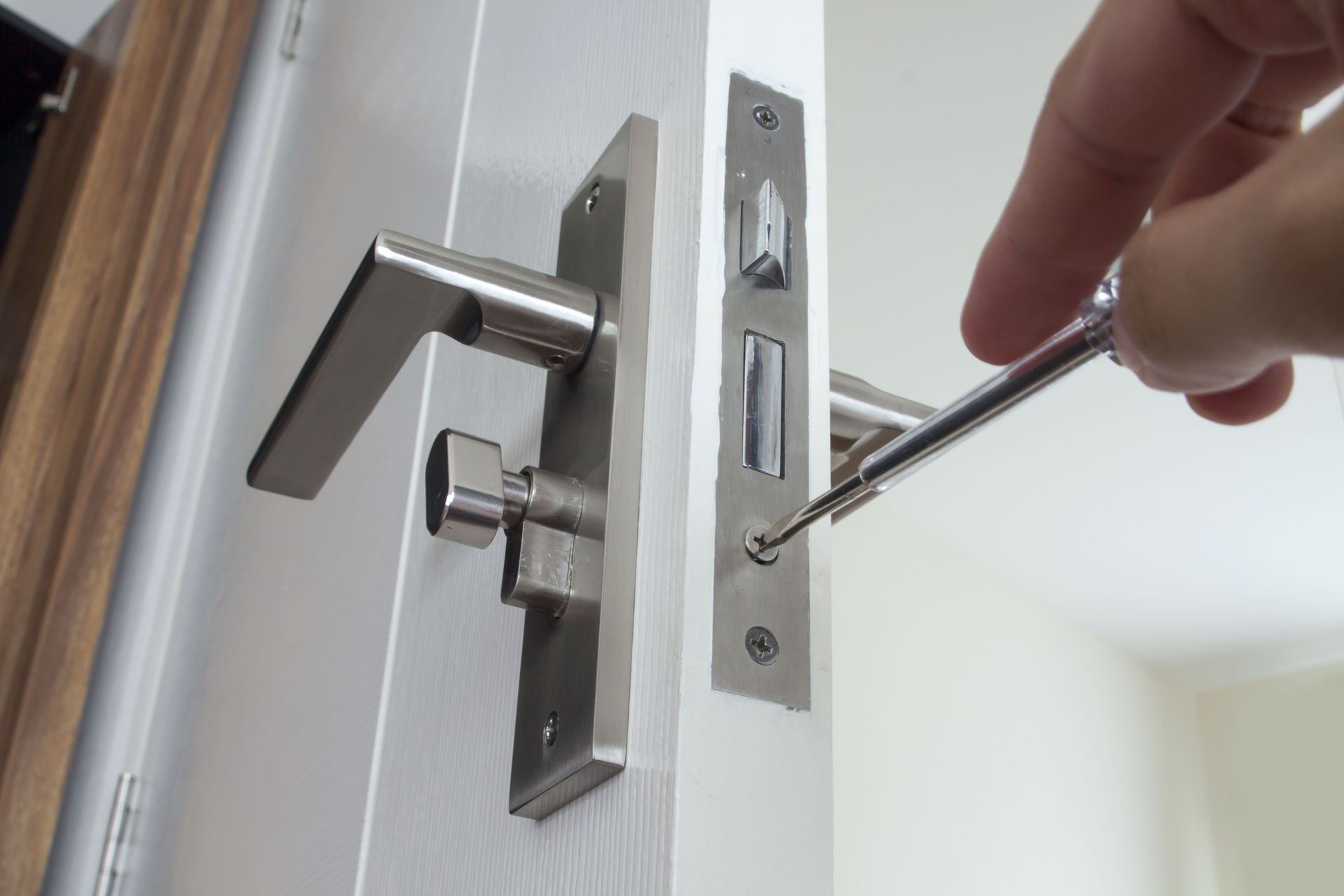 Hand using screwdriver to install or repair a silver door handle on a white door.