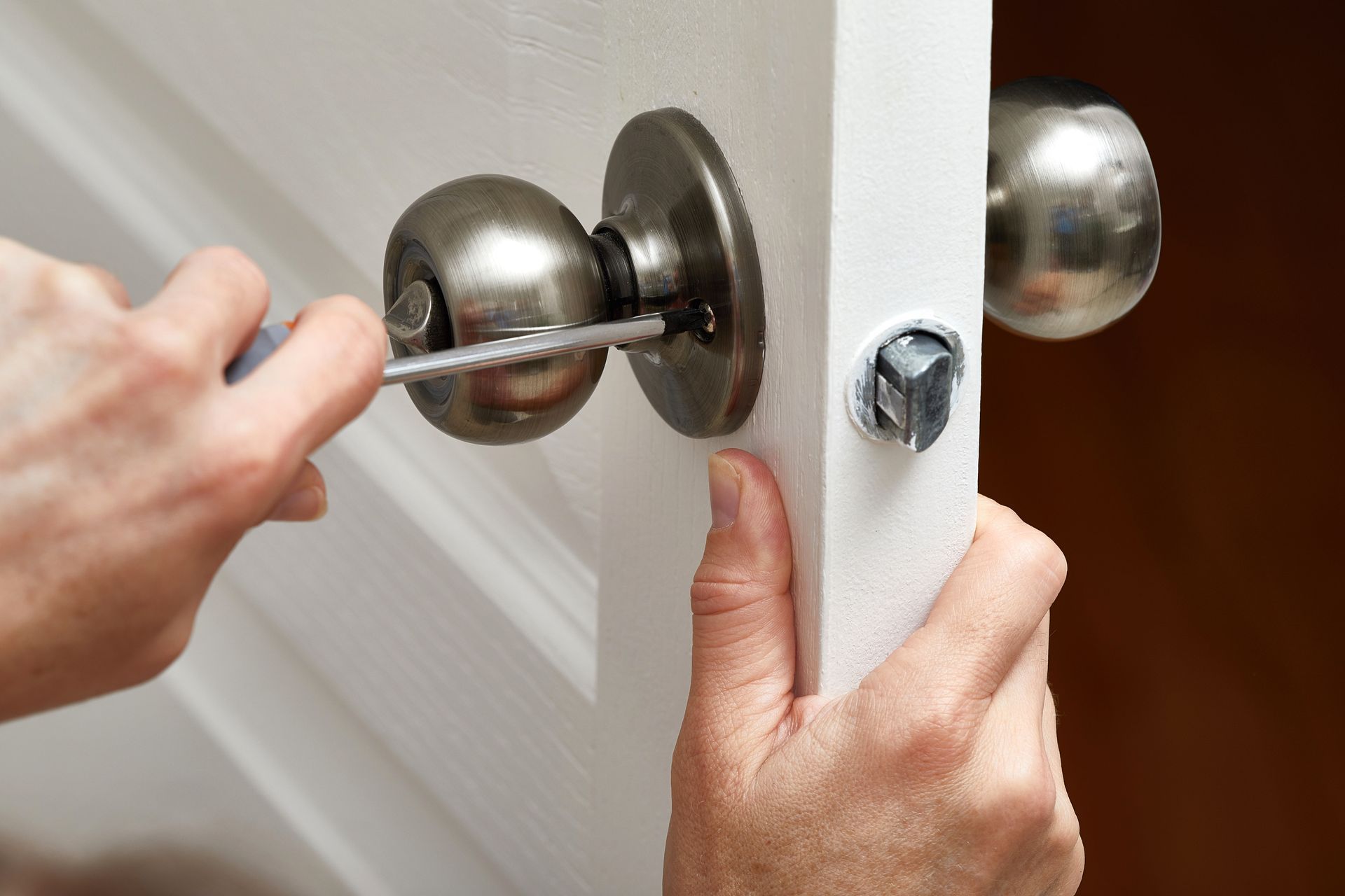 Person using a screwdriver to remove a doorknob from a white door.