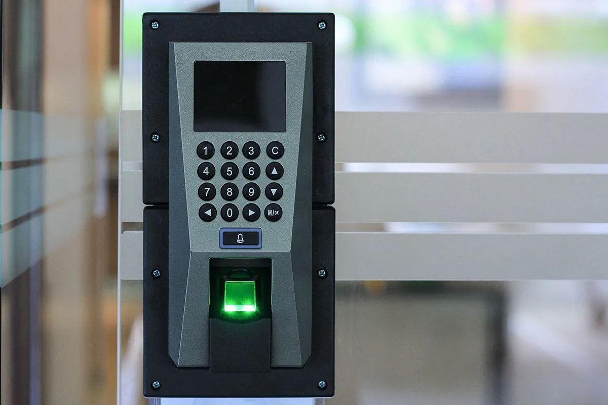 Fingerprint and keypad access control system on glass door. Green light indicates readiness.