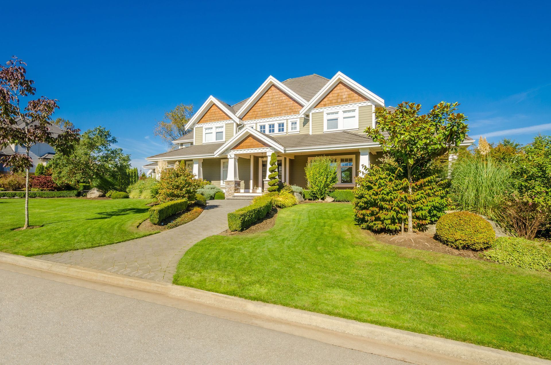 A two-story house with green lawn, trees, and blue sky.