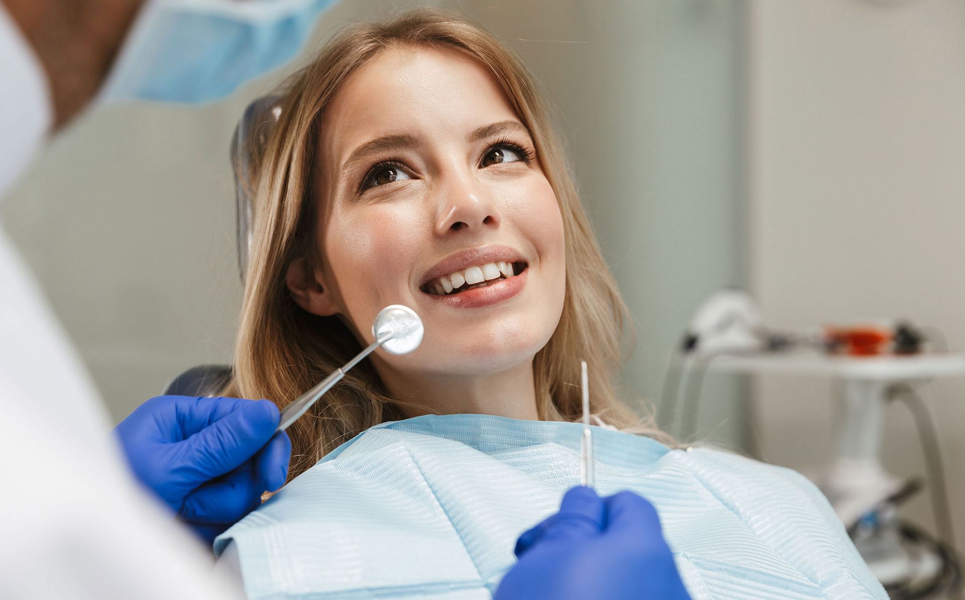 A dentist wearing blue gloves performs an examination on a patient sitting in a dental chair.