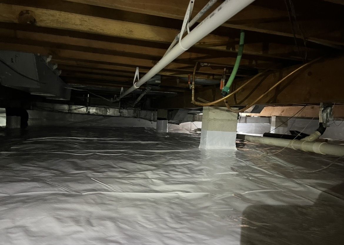 A crawl space with a lot of pipes and wires.