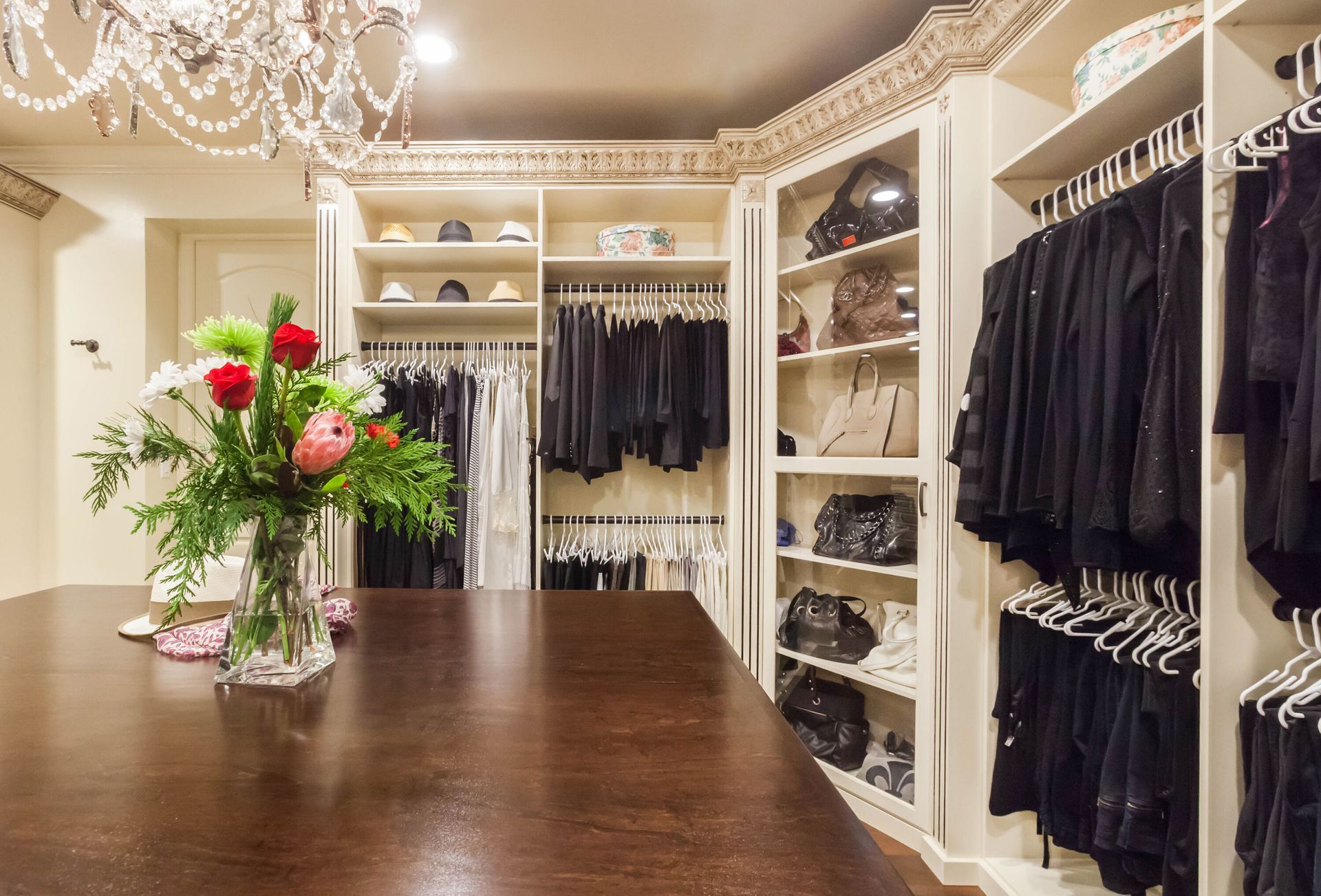 A luxurious walk-in closet with dark wood island, shelves with clothes, and a chandelier.