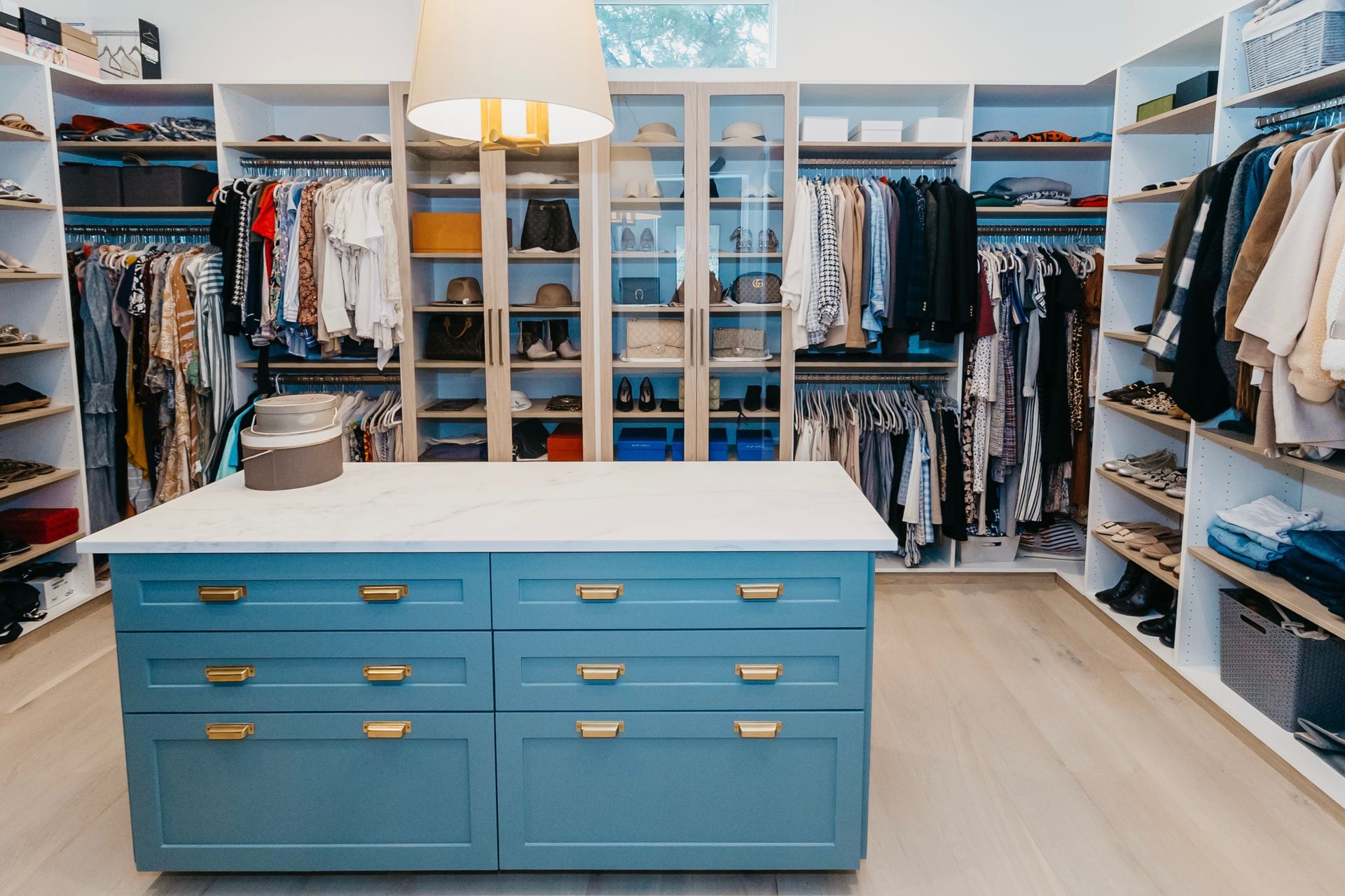 A spacious walk-in closet with a blue island in the center, filled with clothes, shoes, and accessories.