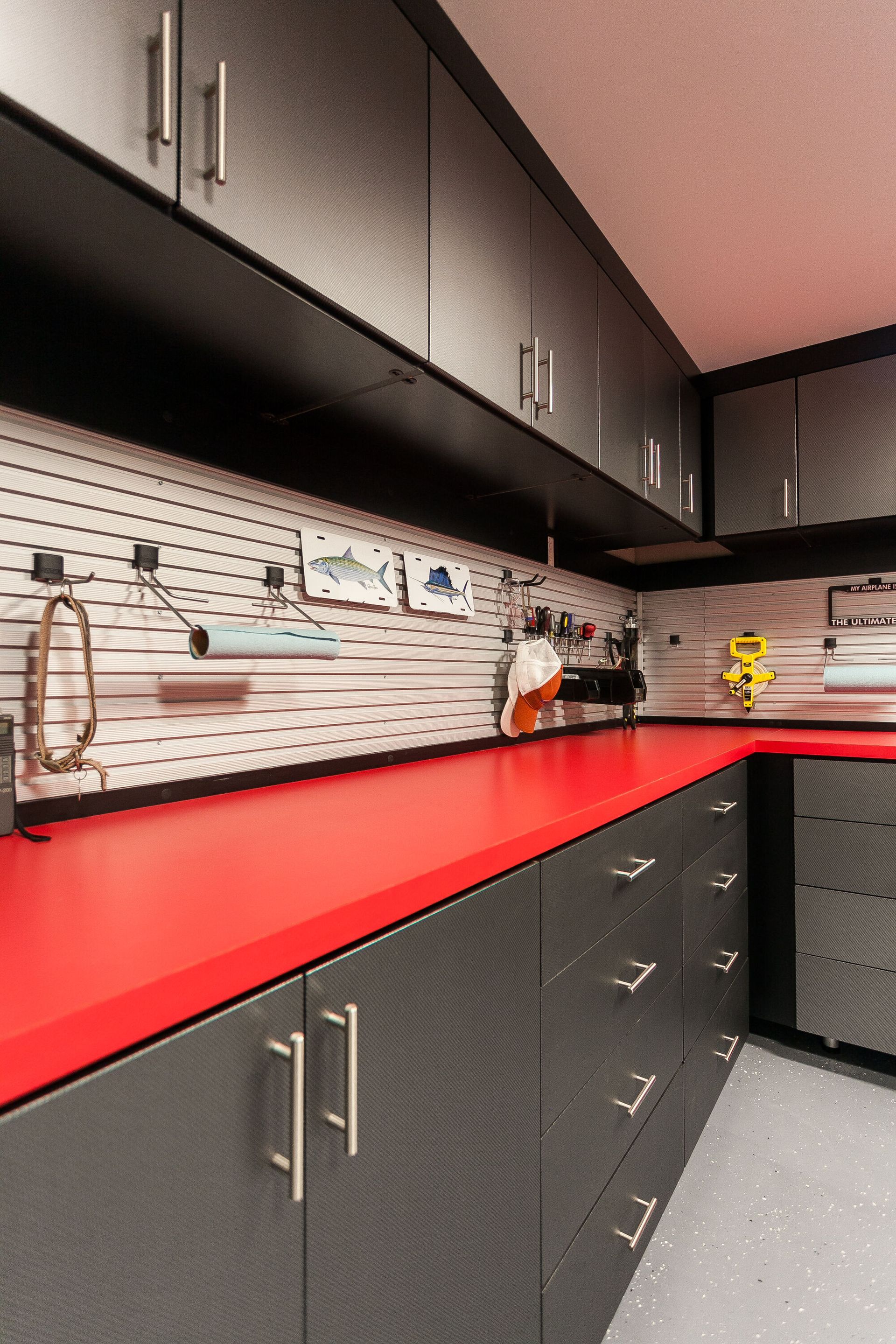 Garage interior with gray cabinets, red countertop, and white slatwall for hanging tools.