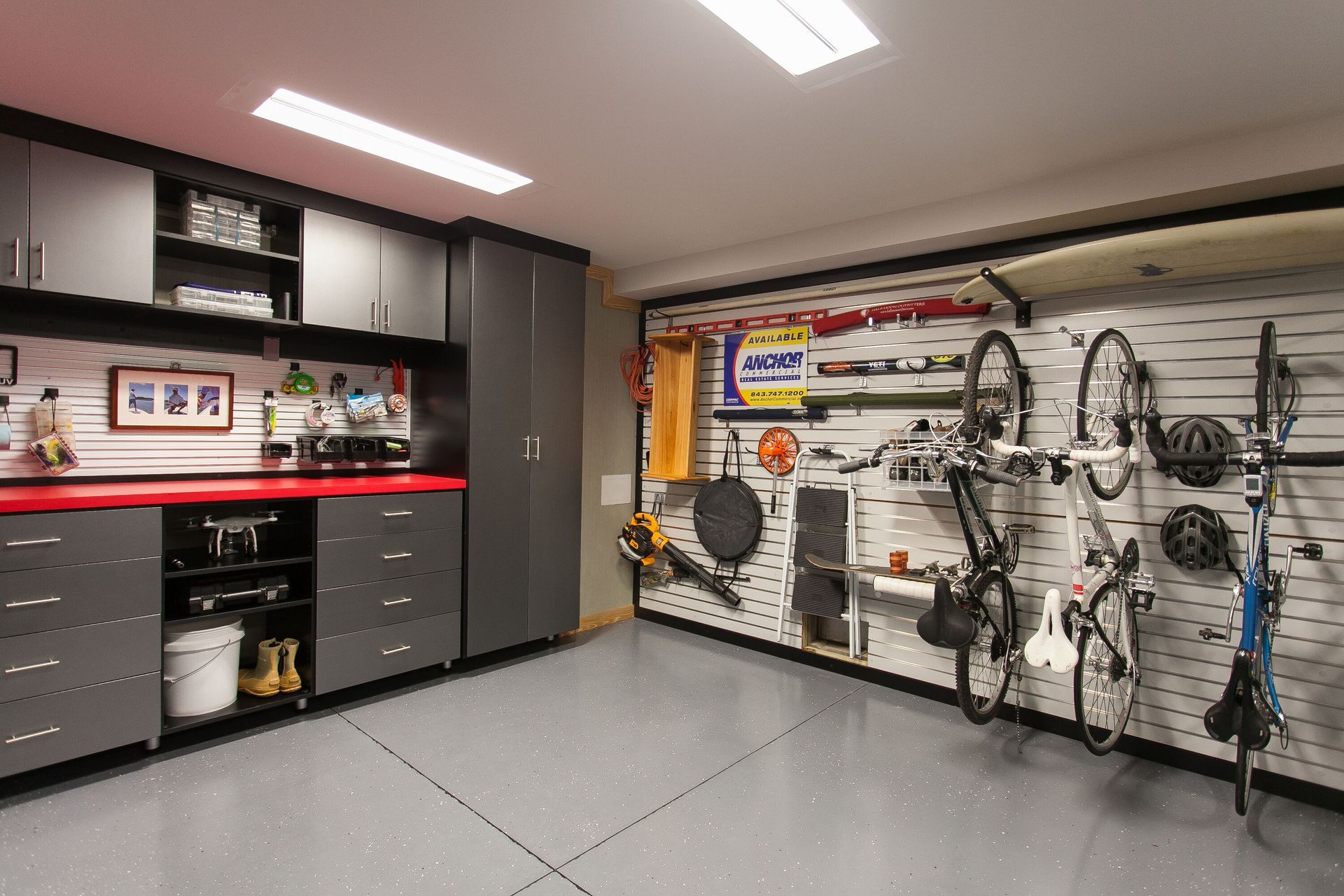 A well-organized garage with gray cabinets, a red countertop, and storage racks holding bicycles and tools.