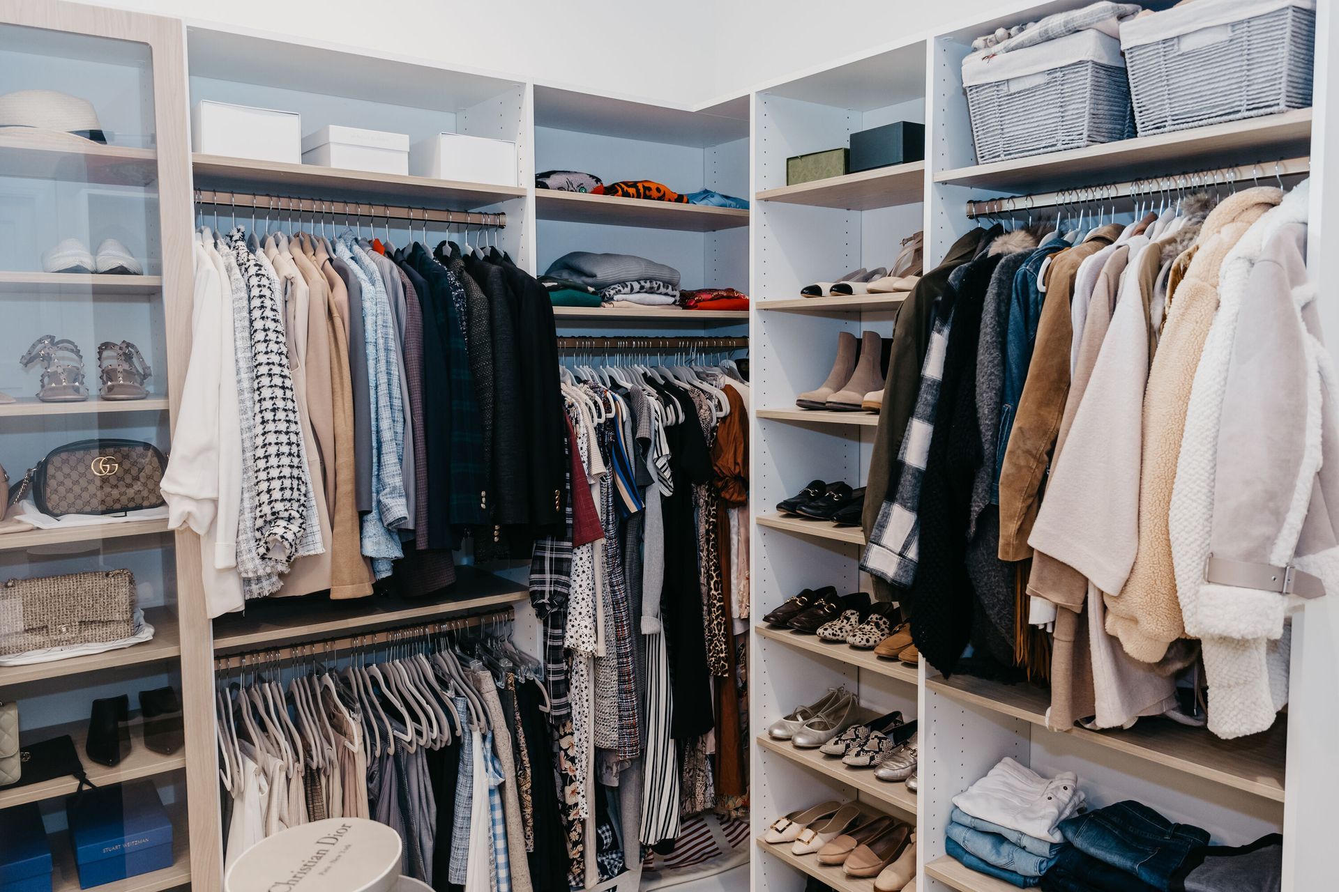 A well-organized walk-in closet with hanging clothes, shelves, and storage boxes. White shelves hold clothing, shoes, and accessories in a bright, clean space.
