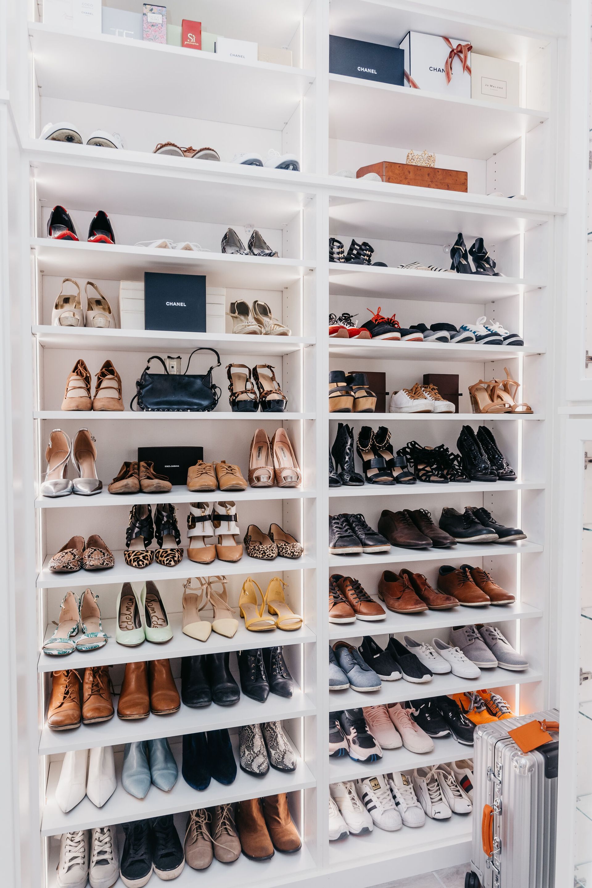 A well-lit, white shoe closet filled with a variety of women's shoes neatly arranged on shelves.