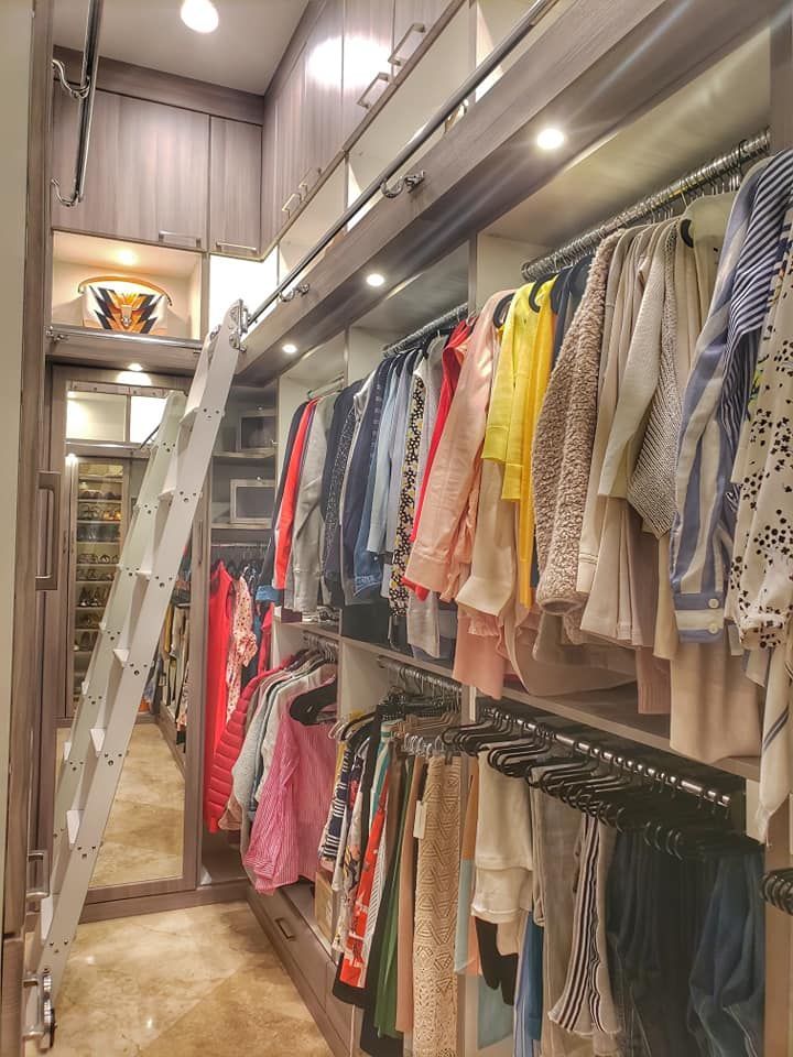 Walk-in closet with a rolling ladder. Rows of clothes hang on racks of various colors, with soft lighting overhead.