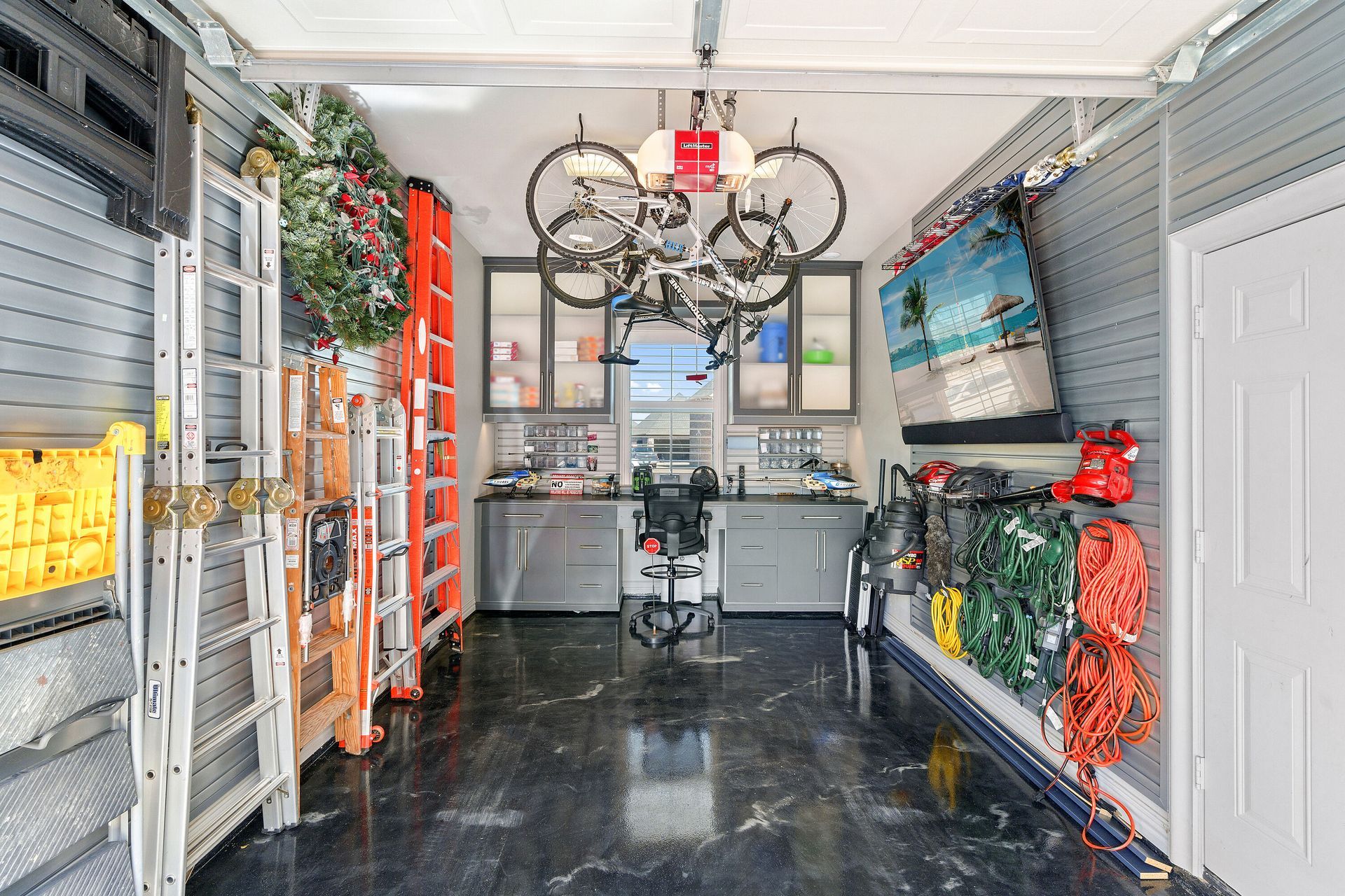 Organized garage interior with storage cabinets, hanging bikes, and tools on the walls.