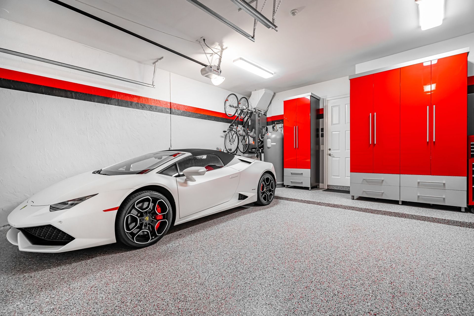 White Lamborghini in a clean, modern garage with red and gray storage cabinets and a bike rack.