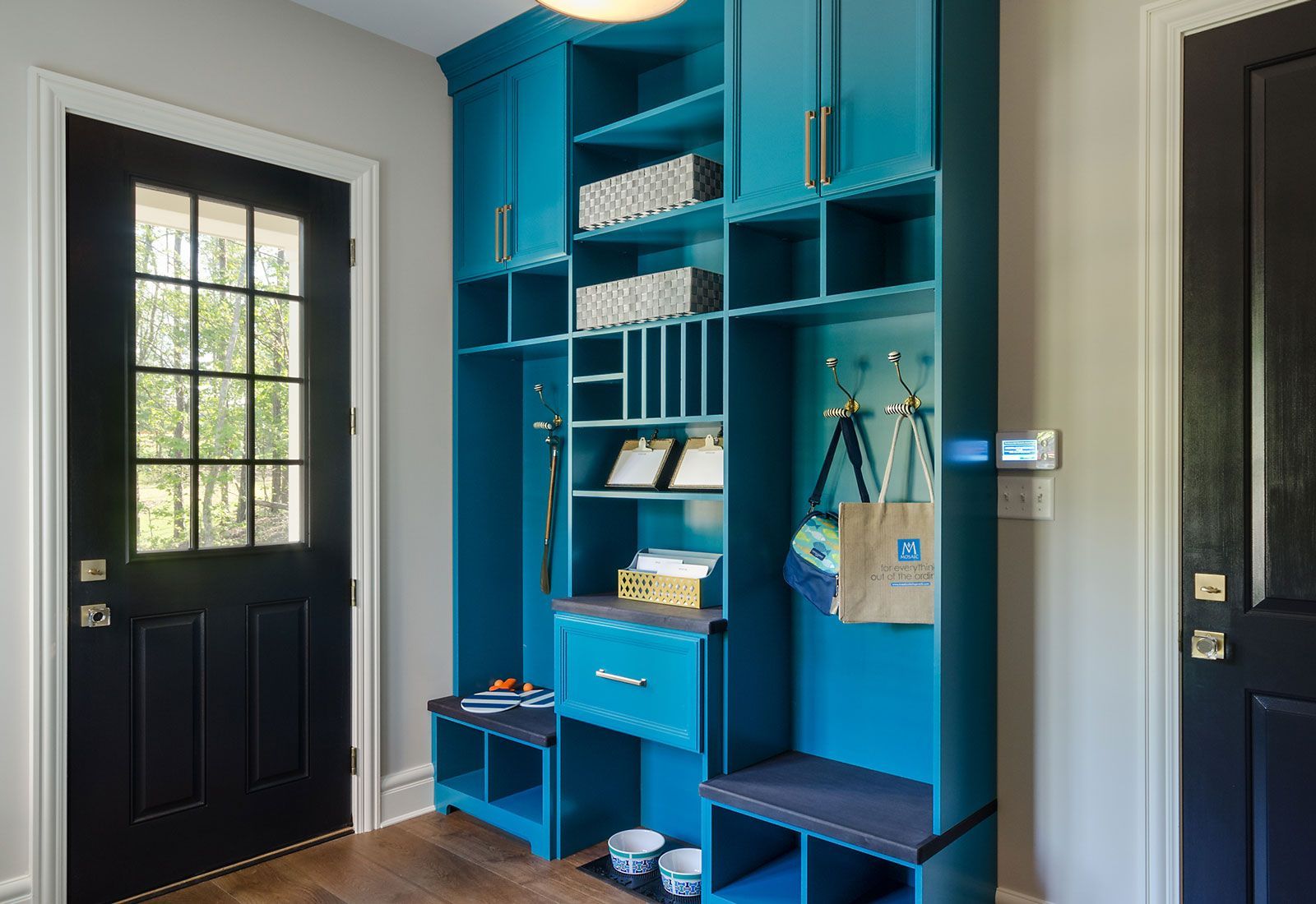 Bright blue built-in entryway storage with cabinets, shelves, and hooks. Includes a bench, drawers, and mail organizer next to a black door.