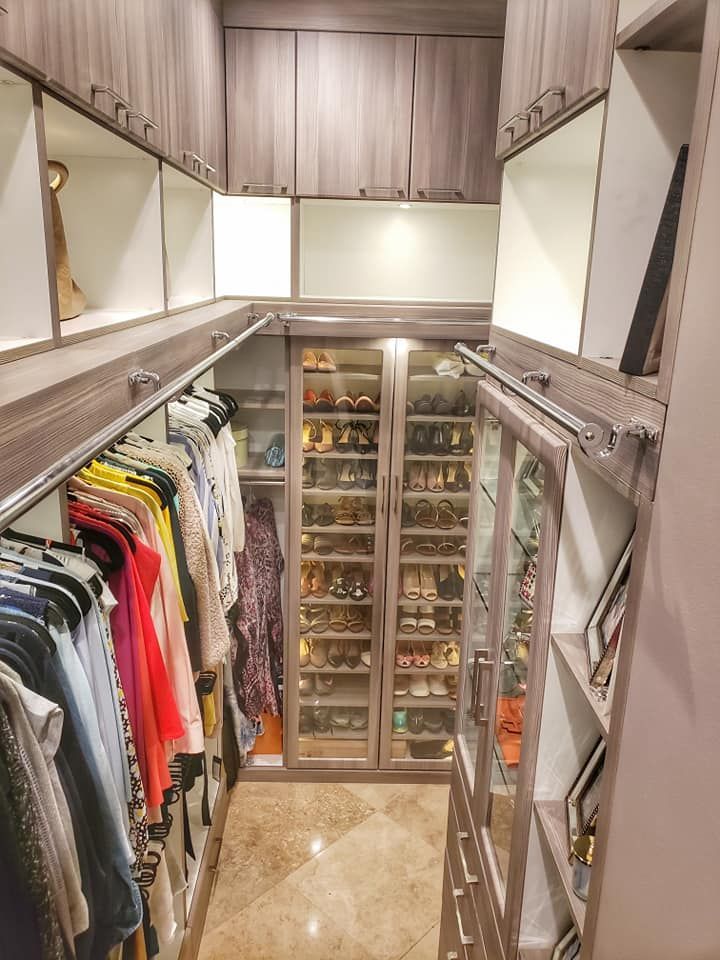 Walk-in closet with built-in shelves and racks for clothes and shoes. Neutral tones with glass-door shoe display.
