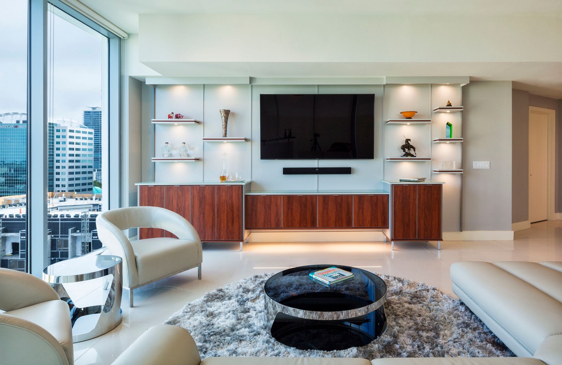 Modern living room with a large window overlooking a cityscape, featuring a built-in entertainment center and stylish furniture.