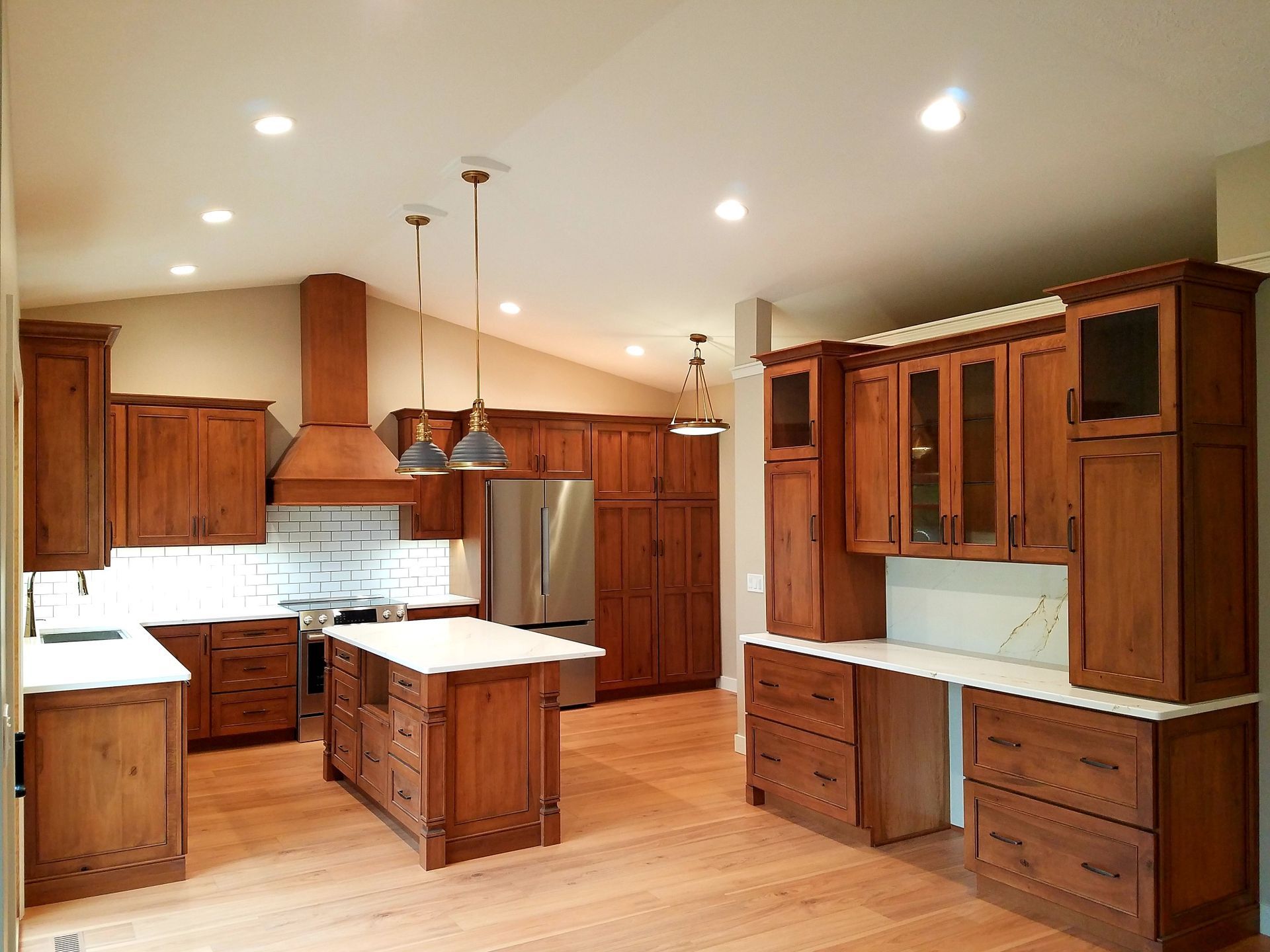 A spacious kitchen with natural wood cabinets, white countertops, a center island, and stainless steel appliances.