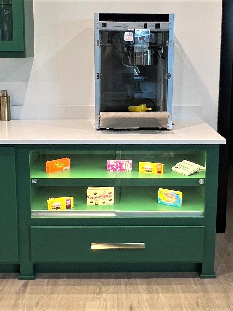 A green display cabinet with a coffee machine on top, housing various packaged snacks on its two shelves.