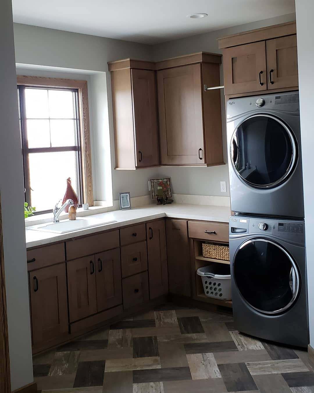 A laundry room with brown cabinets, a window, a white countertop, and a stacked grey washer and dryer set.
