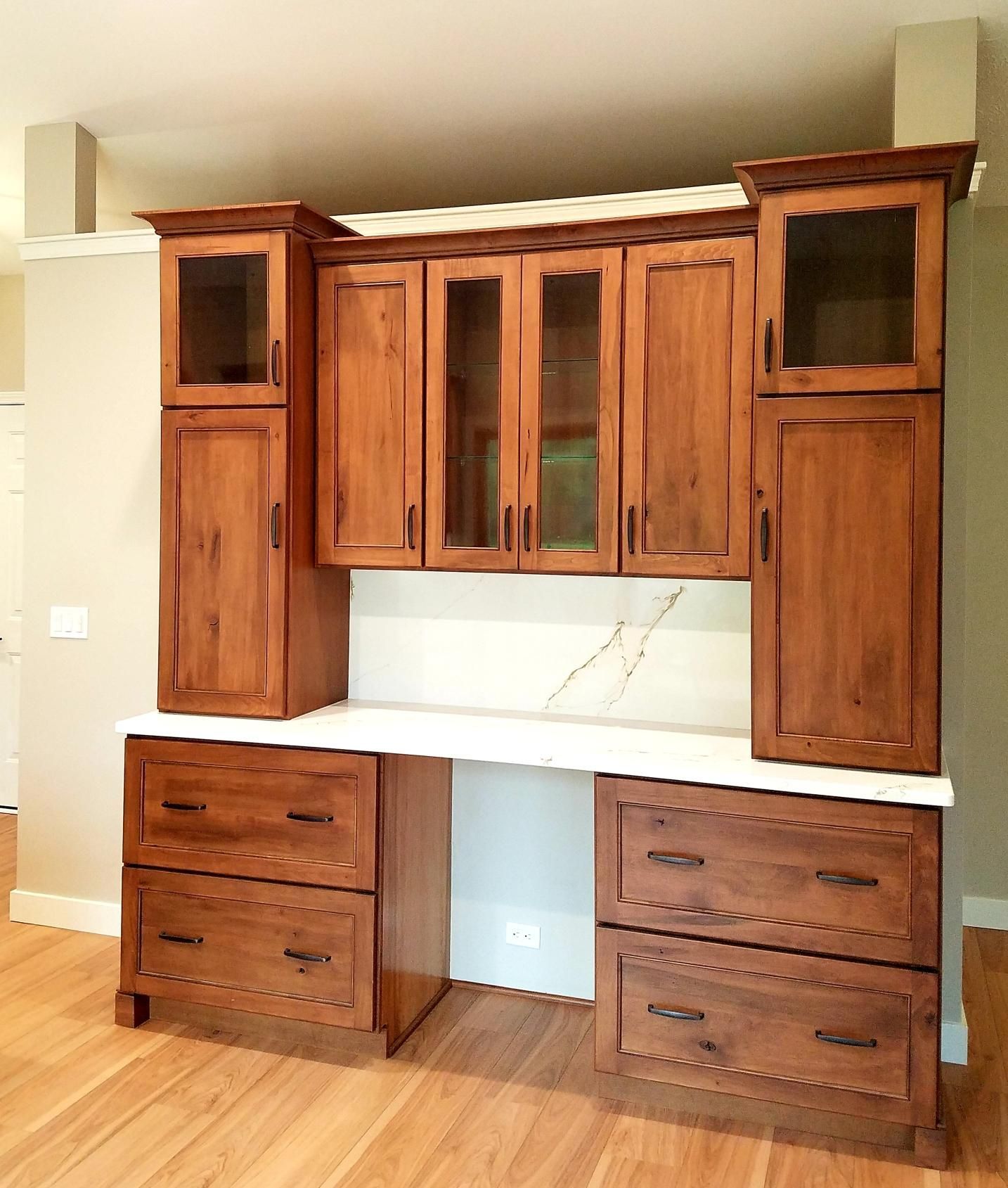 Built-in wooden cabinetry featuring a desk surface, lower drawers, and upper glass-front cabinets in a room with wood floors.