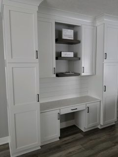 White built-in cabinetry featuring a desk, central open shelving, and tall storage towers on a wood-look floor.