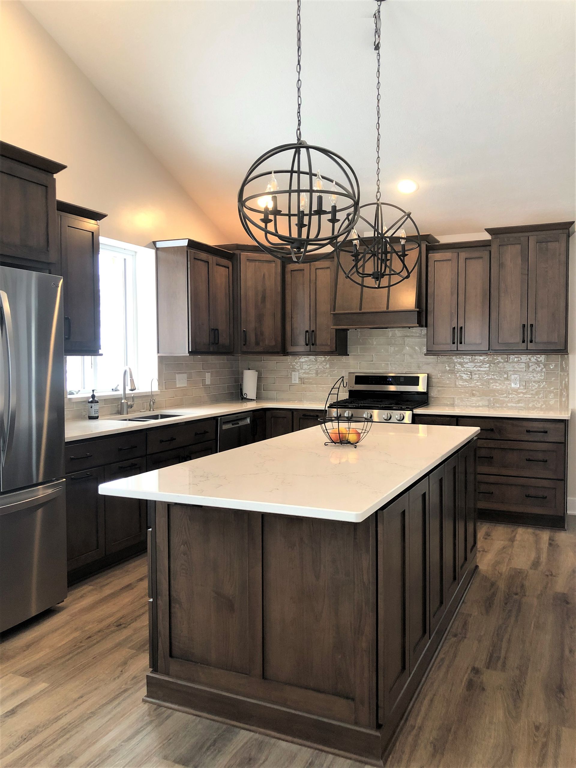 A modern kitchen with dark wooden cabinetry, a white quartz island, stainless steel appliances, and two globe pendants.