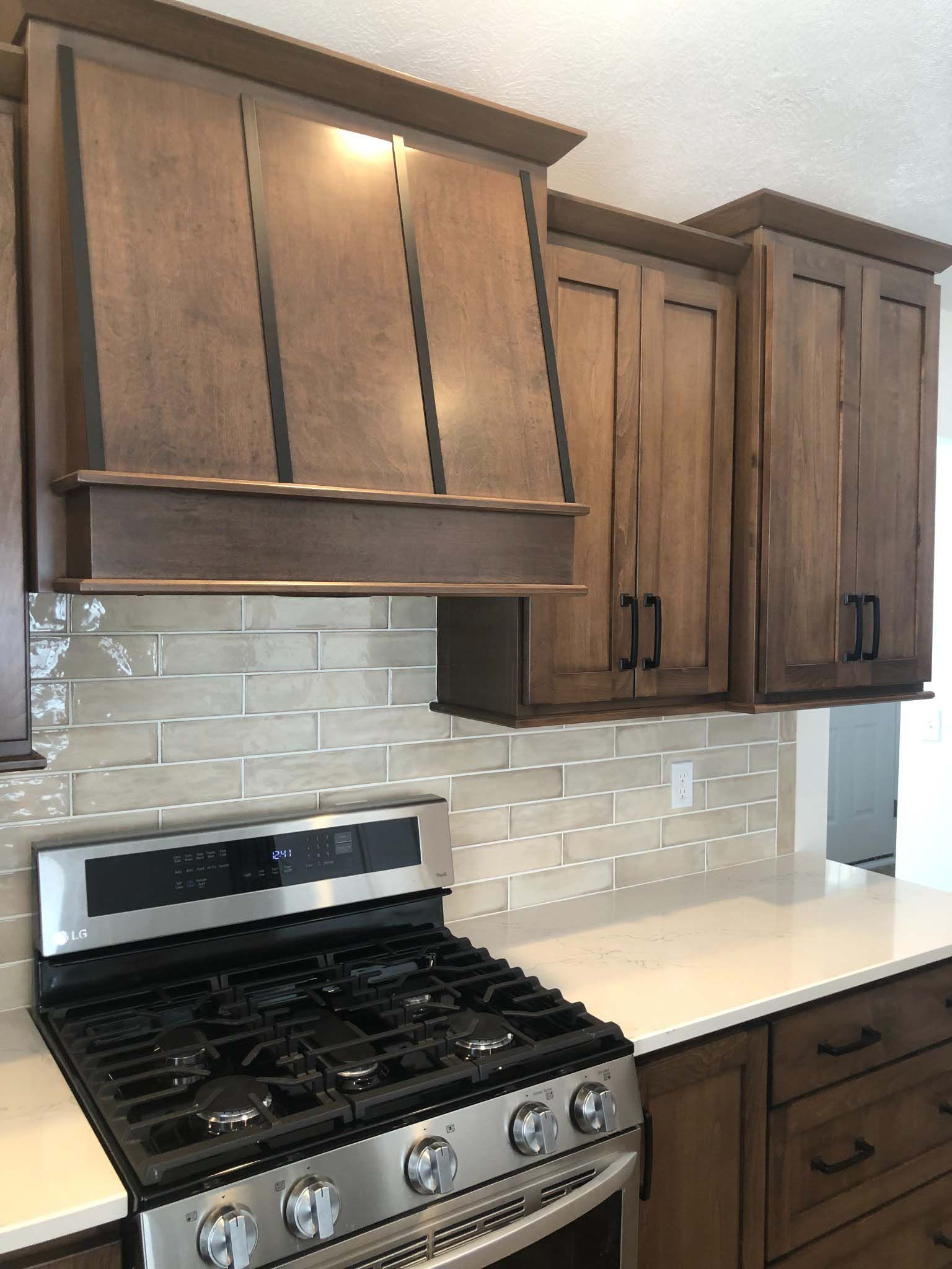 A stainless steel gas stove with a large custom brown wooden range hood above it, flanked by matching dark wood cabinets.