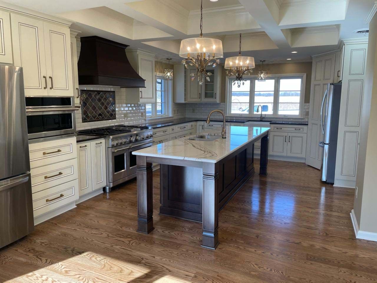 A high-end kitchen with cream cabinets, a dark wood island with white marble countertops, and stainless steel appliances.