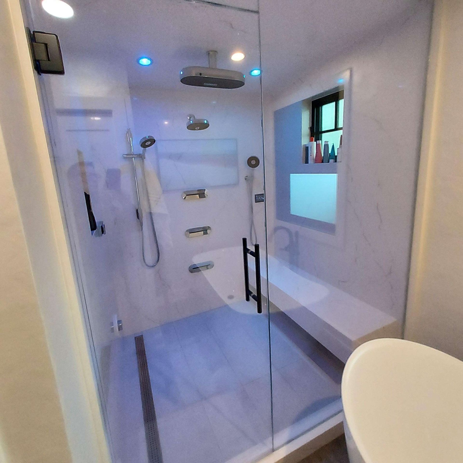 Modern shower stall with marble-patterned walls, a rainfall showerhead, glass door, and a built-in seating bench.