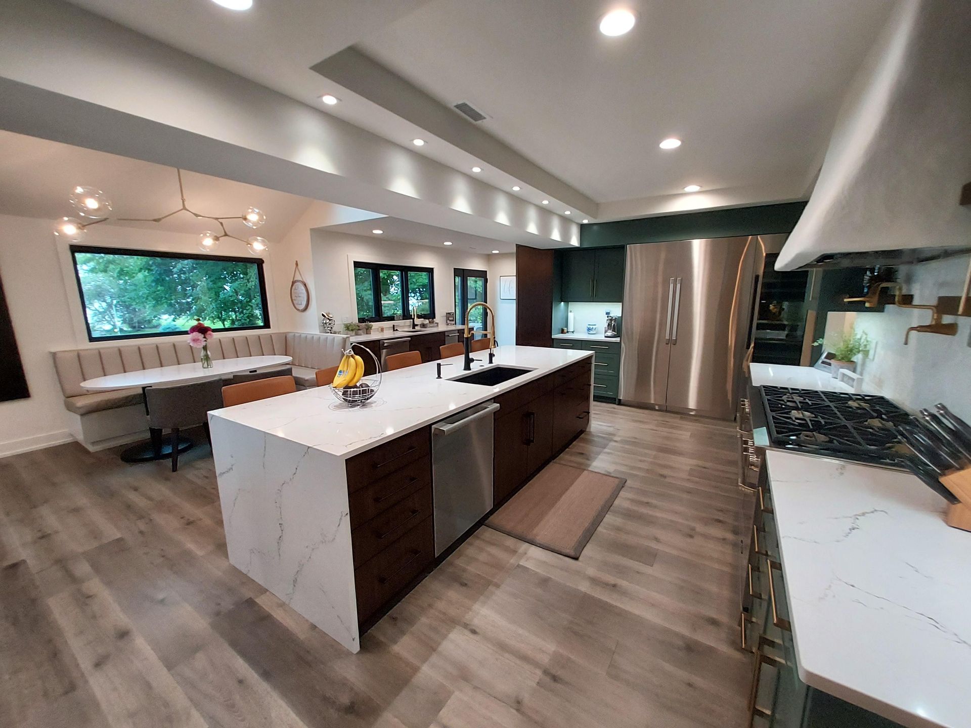 A modern kitchen with dark cabinetry, a large marble-topped island, stainless steel appliances, and a dining nook.
