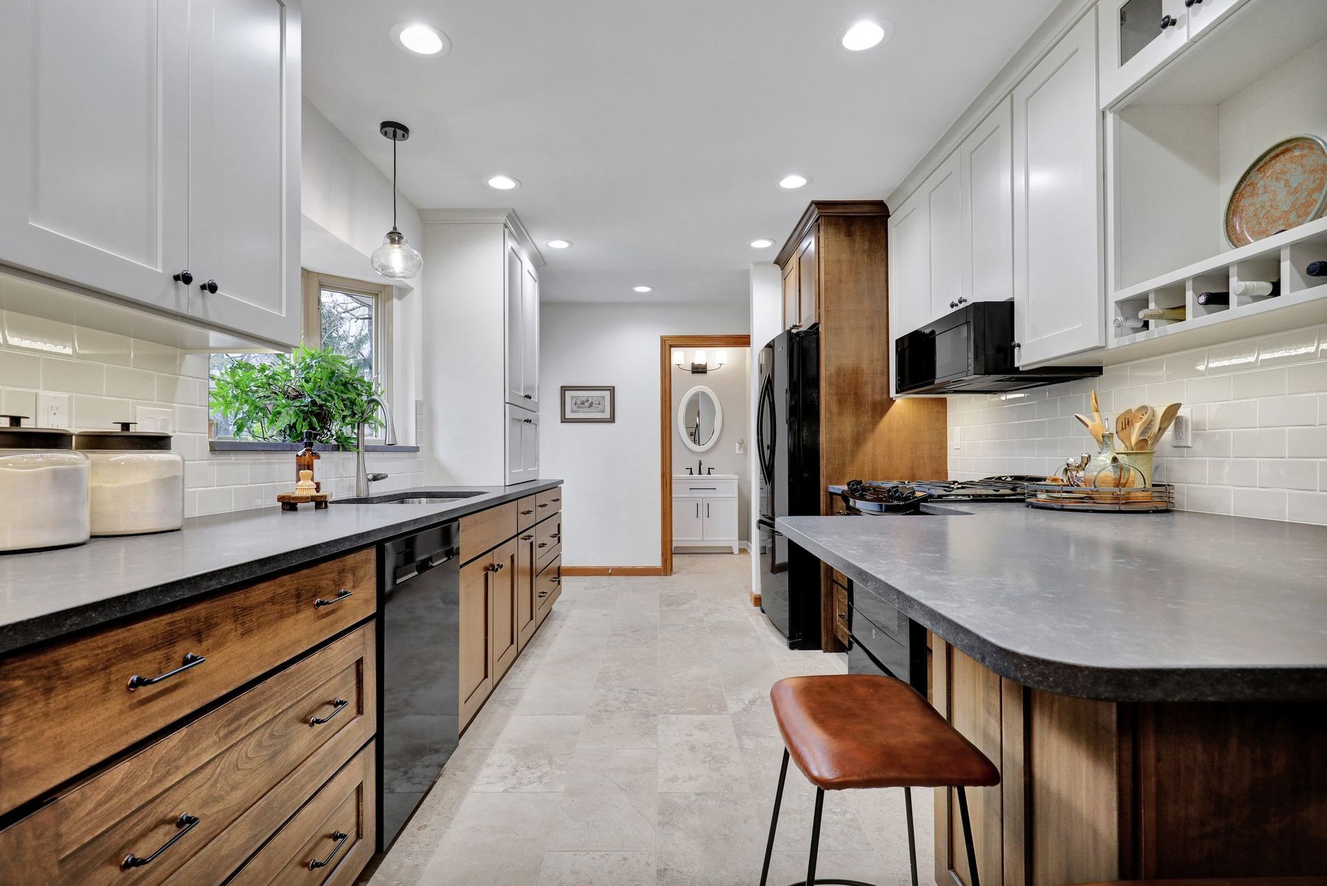 A modern kitchen features white upper cabinets, wood lower cabinets, gray countertops, and a single bar stool.