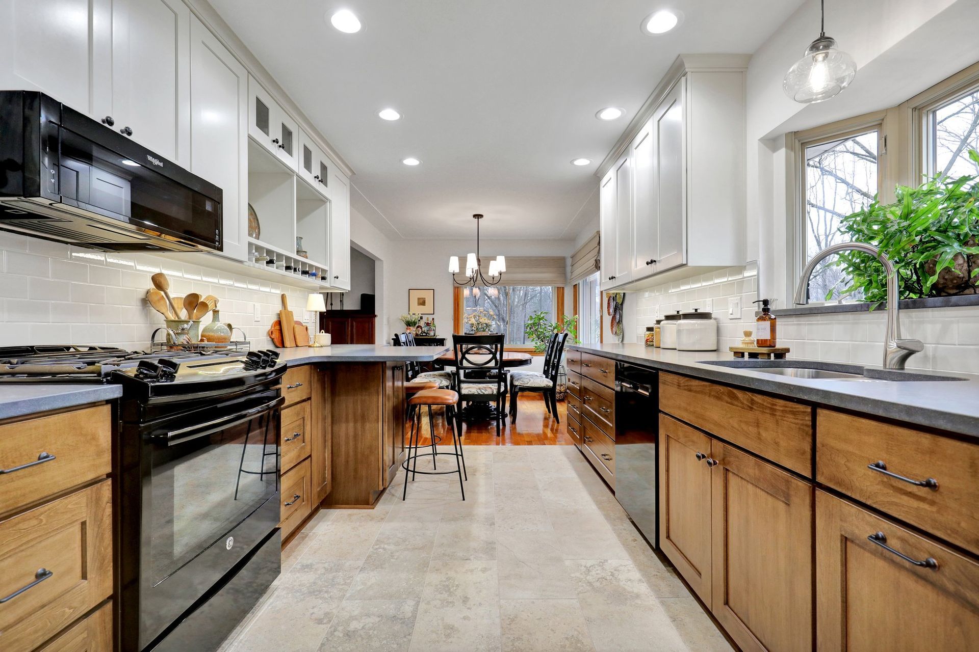 Modern kitchen with wood lower cabinets, white upper cabinets, stainless steel appliances, and a dining area in the back.