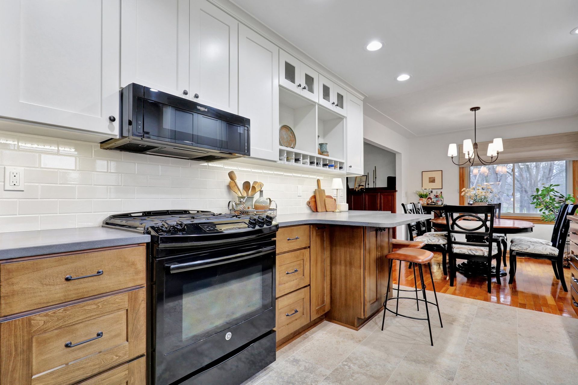 A kitchen featuring white cabinets, a black stove and microwave, wooden drawers, and a view into a dining room.