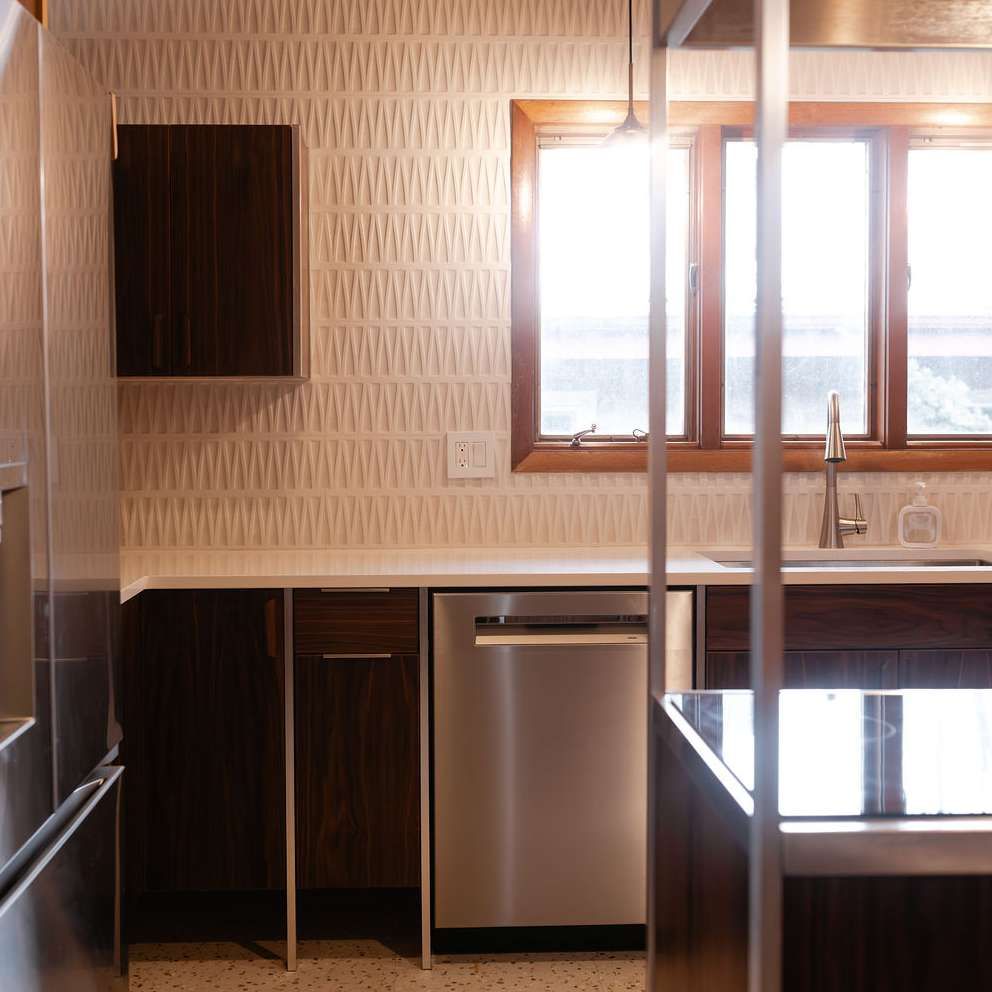 Modern kitchen with dark wood cabinets, light countertops, geometric patterned wallpaper, and stainless steel appliances.
