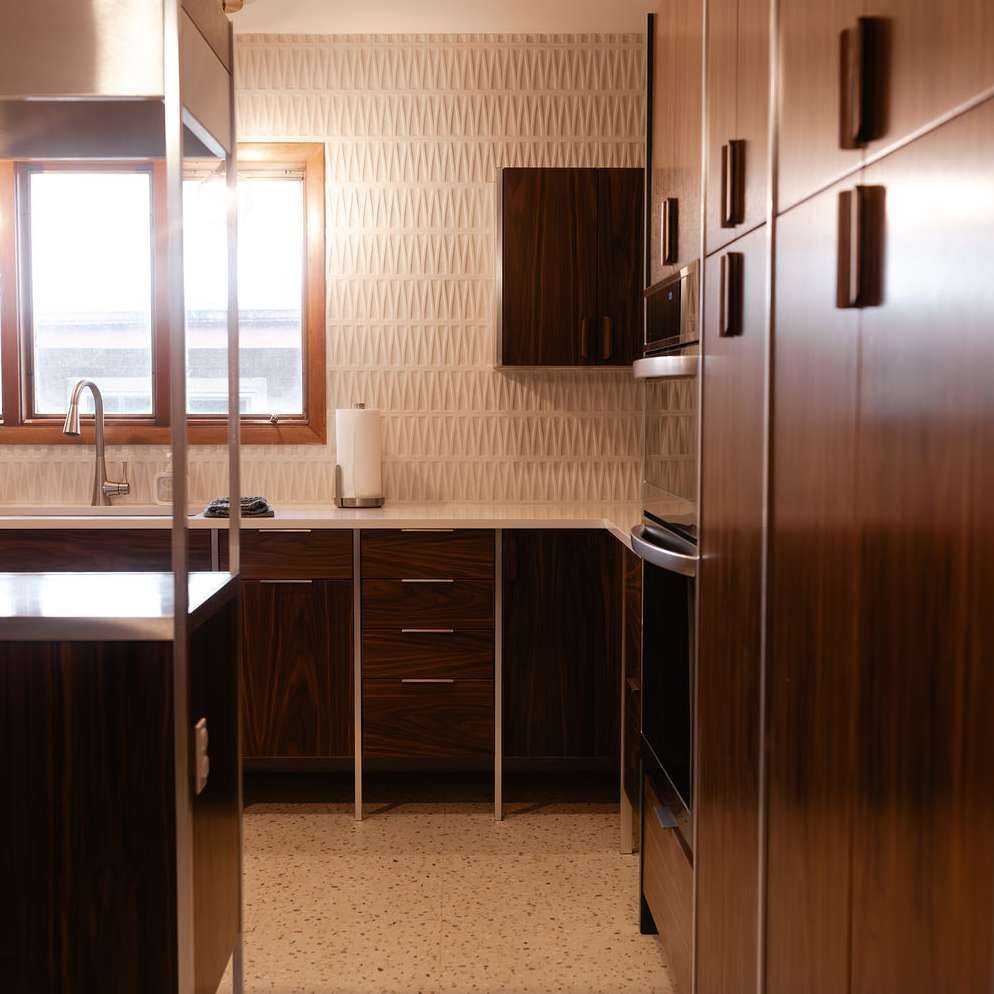 Modern kitchen with dark wood cabinets, white countertops, textured beige wallpaper, and a window above the sink.