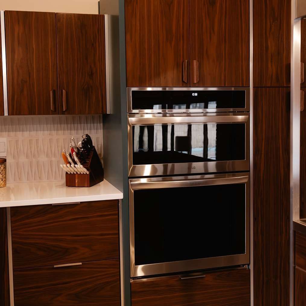 A modern kitchen featuring wood-grain cabinets, a stainless steel wall oven, and a knife block on a white countertop.